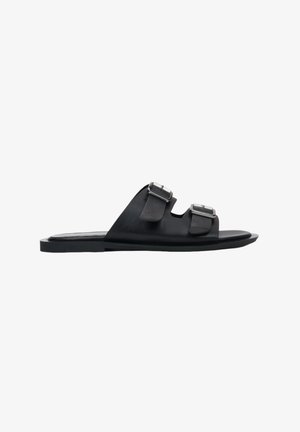 Sandales à glissière en cuir noir avec deux boucles argentées ajustables, design minimaliste, bout ouvert, semelle plate, texture lisse et sans talon.