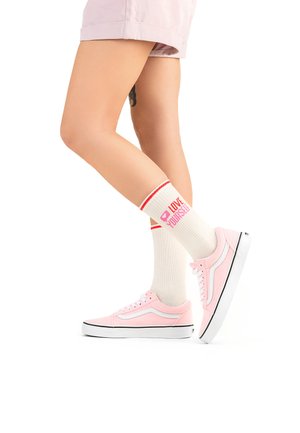 Rosa Leinenschuhe mit weißen Akzenten und schwarzen Sohlen, kombiniert mit cremefarbenen Socken, die rote Streifen und den Text "LOVE YOURSELF" tragen.