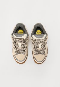 Sneakers bege com atacadores em padrão espinha de peixe, detalhes cinzentos e um cabedal texturizado. Apresentam um bico redondo e sola de borracha. Logotipo visível no interior.