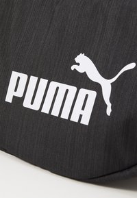 Bolsa de tela negra con una superficie texturizada, gran logotipo blanco de "PUMA" y un gráfico de un gato saltando en blanco, que destaca su diseño deportivo.