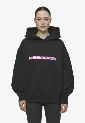 Schwarzer, übergroßer Kapuzenpullover aus weichem Material mit einer Fronttasche. Mit einem auffälligen pinken „DEGADOR“-Logo auf der Brust.