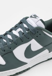 Low-top Nike sneaker in dark green and white, featuring thick laces and a stitched Nike swoosh on the side.