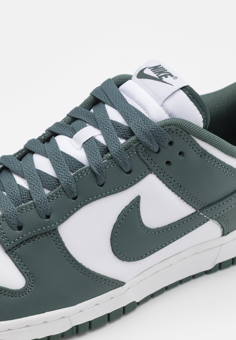 Lage Nike sneakers in donkergroen en wit, met dikke veters en een gestikte Nike swoosh aan de zijkant.