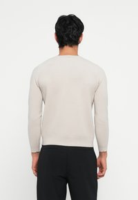 Suéter de malha bege claro com mangas longas e decote redondo. Apresenta uma textura suave e um design ajustado. Usado com calças pretas.