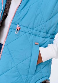 Světle modrá prošívaná vesta s růžovým zipem a akcenty. M�á měkkou šedou podšívku a boční kapsu. Texturovaný, lehký materiál.