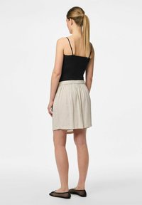 Czarna bluzka na cienkich ramiączkach, beżowa spódnica do kolan z elastycznym pasem i czarne płaskie buty z siateczki, widok z tyłu. Gładka tekstura.