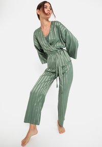 Groene gestreepte loungewear set met een wikkelstijl top met striksluiting en een brede broek, gemaakt van een gladde, glanzende stof.