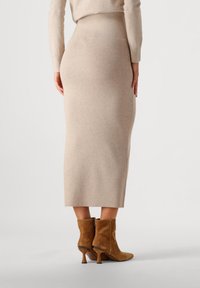 Fustă midi tricotată ribbed de culoare bej, cu un talie ajustată, asortată cu cizme scurte din suede maro, cu toc conic și detaliu cu fermoar.