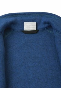 Niebieski kołnierz z polaru o miękkiej, teksturowanej powierzchni. Zawiera metkę z napisem "Byłem tutaj", z kontrastującymi czarnymi detalami.