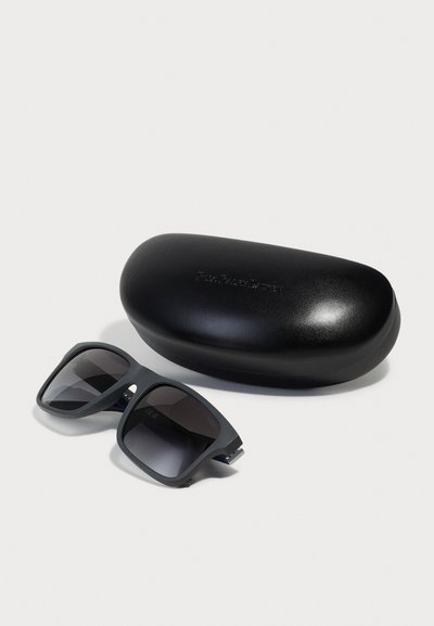 Sonnenbrille mit dunklen Gläsern, grauen geometrischen Rahmen und silbernen Akzenten, sowie einem schwarzen Hartschalenetui mit glatter Oberfläche.