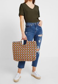 Flerfarvet vævet tote bag med et mønstrede design, top håndtag og en bred åbning. Materialet virker solidt med en tekstureret overflade.