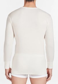 Maglietta termica a maniche lunghe, di colore crema, realizzata in tessuto morbido, con scollatura tonda e silhouette aderente, caratterizzata da polsini a costine.