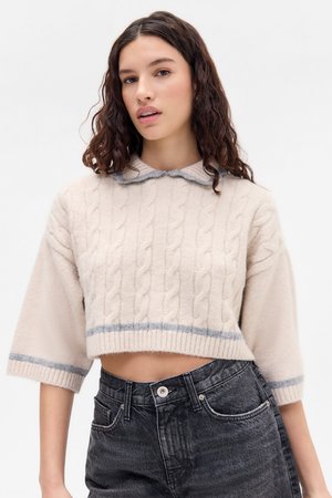 Beiger, kurz geschnittener Pullover mit Kabelstrickmuster, geripptem Saum und hellgrauem Kragen. Kombiniert mit dunkelblauen, hoch sitzenden Jeans.