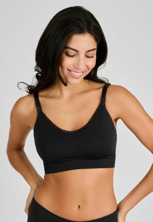 Musta langaton bralette, joka on valmistettu pehmeästä kankaasta, jossa on säädettävät hihnat, pitsikoriste kaula-aukossa ja saumatonta muotoilua.