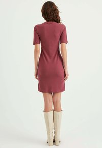 Ribbet strikkjole i dæmpet bordeaux, med korte ærmer og en tætsiddende silhuet, parret med knæhøje beige støvler.
