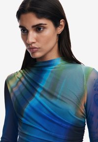 Blå och grön långärmad topp gjord av lättviktsmaterial har draperad textur och abstrakt mönster med subtila färggradienter.