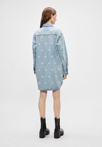 Heled sinine denim kleit korduva logo mustriga, pikad varrukad ja krae. Koos mustade paksude pahkluu saapatega. Sile tekstuur, juhuslik lõige.