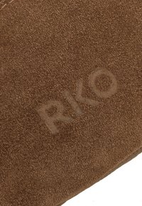 Primer plano de cuero de gamuza marrón suave con el nombre de la marca "RIKO" grabado en diagonal sobre la superficie.
