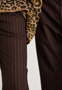 Knit sweater with a leopard pattern in gold and green, paired with brown pinstriped trousers. Fabrics are soft and textured.
