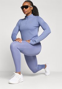 Lys blå atletisk langærmet bluse med lynlås krave, parret med matchende tights. Hvide sneakers og solbriller fuldender looket.