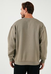 Sudadera verde oliva de corte relajado, con puños y cuello de canalé. Tejido suave con un acabado texturizado, presenta detalles de costura.