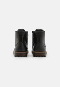 Botas de tobillo de cuero negro con un acabado suave, que cuentan con una cremallera en el lateral, tacón bajo y suela de goma marrón con dibujo texturizado.