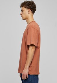 Kostkované tričko z bavlny v rustické barvě s krátkými rukávy, kulatým výstřihem a uvolněným střihem. Postranní rozparek přidává jemný designový prvek.