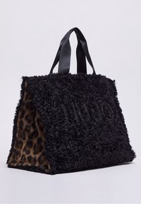Czarna torba tote z faux futra z leopardzim wzorem wewnątrz, posiadająca czarne materiałowe uchwyty i teksturowaną powierzchnię. Logo ozdobione błyszczącymi detalami.