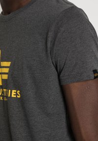 Grey cotton t-shirt with short sleeves, featuring a yellow graphic design and text on the front, and a black tag on the sleeve.