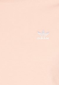 Light pink cotton t-shirt featuring a small embroidered white adidas logo on the left chest. Crew neck design with a smooth texture.