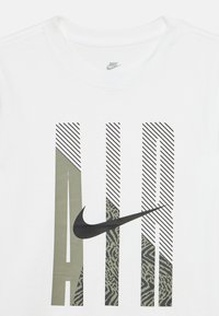 Λευκό T-shirt της Nike με μεγάλο κείμενο "AIR" σε σχέδιο με μοτίβα και ρίγες, έχοντας έναν μαύρο σήμα Nike που διασχίζει τα γράμματα.