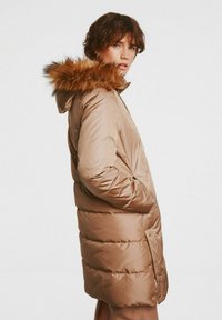 Brązowa kurtka puchowa z kapturem wykończonym futrem, o gładkiej teksturze, z bocznymi kieszeniami i średniej długości.