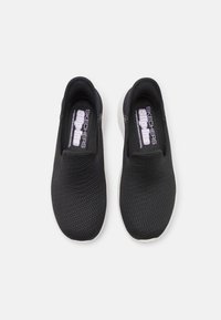 Czarne buty wsuwane wykonane z siateczkowego materiału, z fakturowaną powierzchnią i białą gumową podeszwą. Logo "SKECHERS slip-ins" na wkładce.