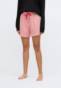 Rode gestreepte shorts met kleine hartjes, elastische tailleband en trekkoord. Gekleed met een zwart top met lange mouwen. Zichtbare blote voeten.