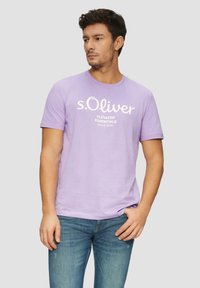 Fialové tričko s krátkým rukávem a kulatým výstřihem, zdobené bílým textem "s.Oliver ELEVATED ESSENTIALS SINCE 1969." Hladká textilie.