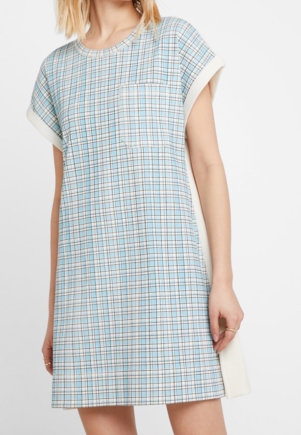 Femme portant une robe à manches courtes, longueur genou, avec un motif à carreaux bleu et blanc et une poche poitrine.