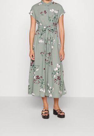 Green floral midi dress with short sleeves, button-up front, and tied waist, worn with black platform sandals with flower details.