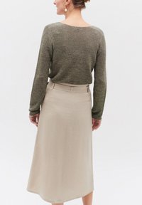 Pull à rayures vert olive avec un tricot texturé et des manches longues, associé à une jupe beige longueur genoux avec une taille ajustée et des poches arrières.