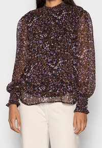 Durchsichtige schwarze Bluse mit lebhaften lila und braunen Blumenmustern, hohem Kragen und gerafften Manschetten mit elastischen Details.