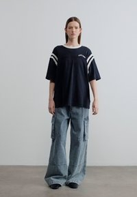 Μαύρο φαρδύ t-shirt με λευκές ρίγες στα μανίκια, συνδυασμένο με ψηλόμεσο, χαλαρό γκρι cargo παντελόνι με τσέπες και φθαρμένη υφή.