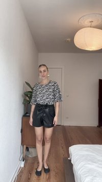 Calções pretos de imitação de pele com uma cintura atada, combinados com uma blusa de padrão zebra em preto e branco. Sapatos pretos simples completam o visual.