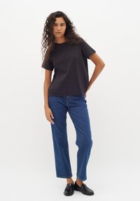 T-shirt en coton noir avec col rond, associé à un jean bleu droit et des mocassins noirs. Le modèle présente une coupe décontractée et une texture naturelle.