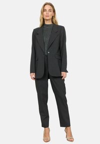 Dunkelgrauer Blazer mit Reverskragen, Ein-Knopf-Verschluss und zwei vorderen Taschen, kombiniert mit passenden, taillierten Hosen und einem strukturierten Oberteil.