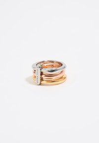 Stacked rings in silver, rose gold, and yellow gold tones, featuring smooth, rounded shapes with a polished finish. Include a small tag detail.
