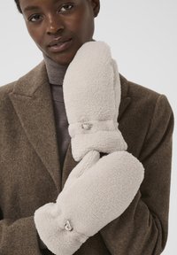 Mănuși din blană albă, ținute aproape, cu o textură moale, formă rotundă și un buton mic ca accent pe manșetă.