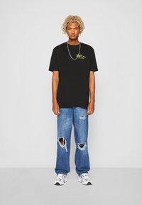 Svart bomull T-skjorte med korte ermer, med neonlys grafisk tekst; paret med lyseblå slitte jeans og hvite sneakers.