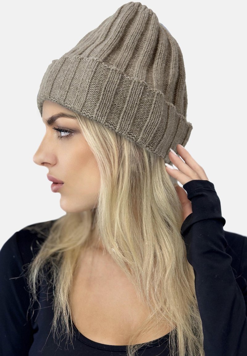Gorro de punto beige con acanalado vertical. Textura suave, con puño doblado y forma ligeramente cónica. Lo lleva una persona con cabello largo y rubio.