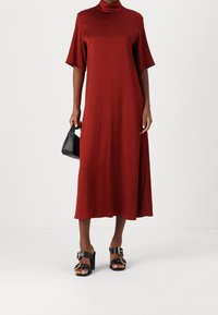Vestido midi rojo con cuello alto, mangas cortas y una textura suave. Combinado con sandalias negras de tacón con hebillas y un bolso pequeño.