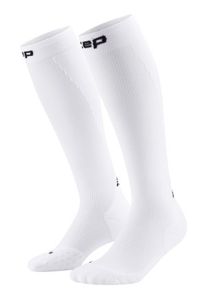 Kniestrümpfe aus Kompressionsmaterial in Weiß, aus geripptem Stoff, mit einem schwarzen Logo oben und einer strukturierten Sohle für einen besseren Halt.