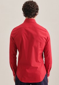 Chemise rouge à manches longues en tissu lisse. Présente un col boutonné, un ourlet droit et des poignets à boutons. Design simple sans motifs.